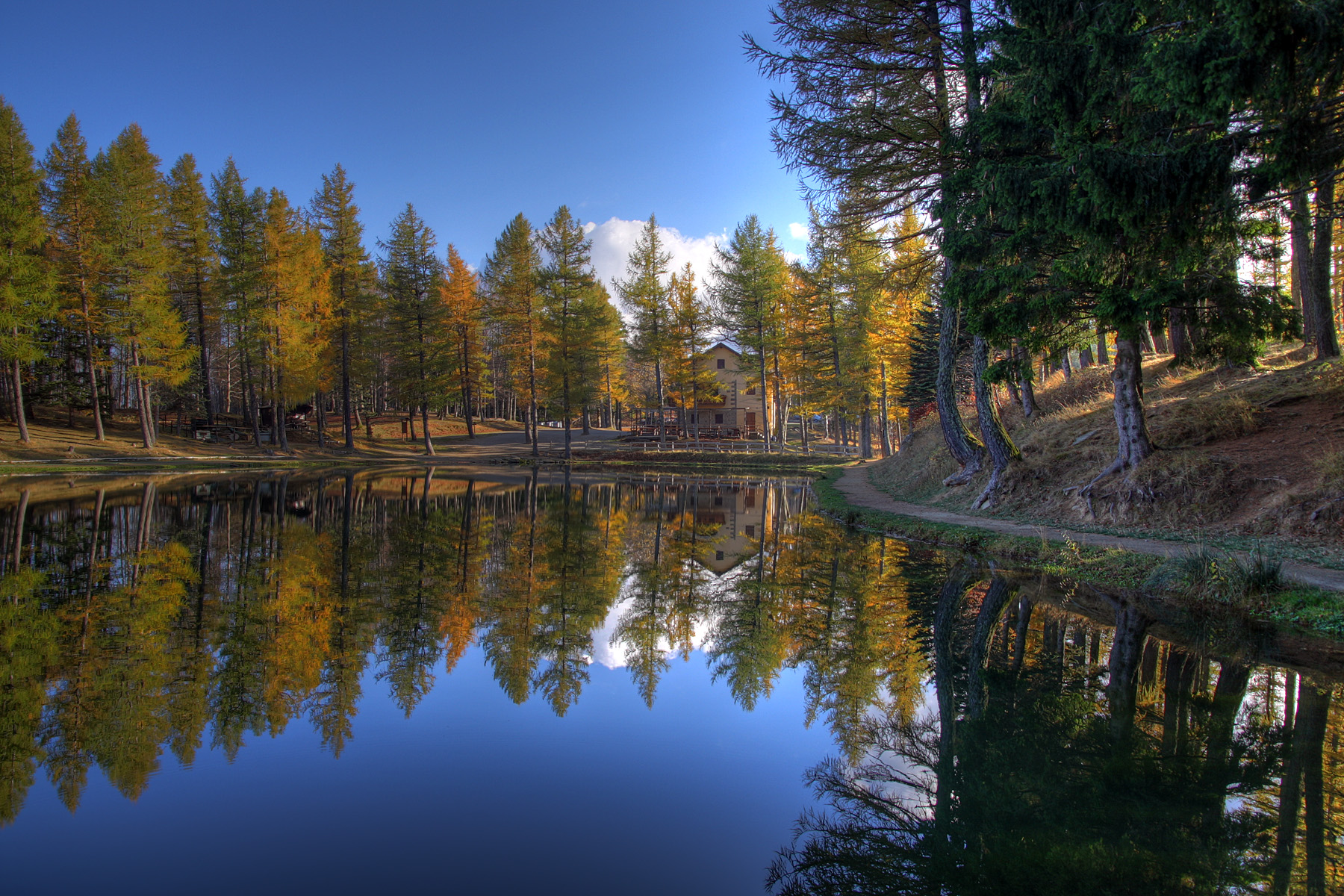 Il Lago della Ninfa riflette i larici e i faggi colorati d'autunno sotto un cielo azzurro