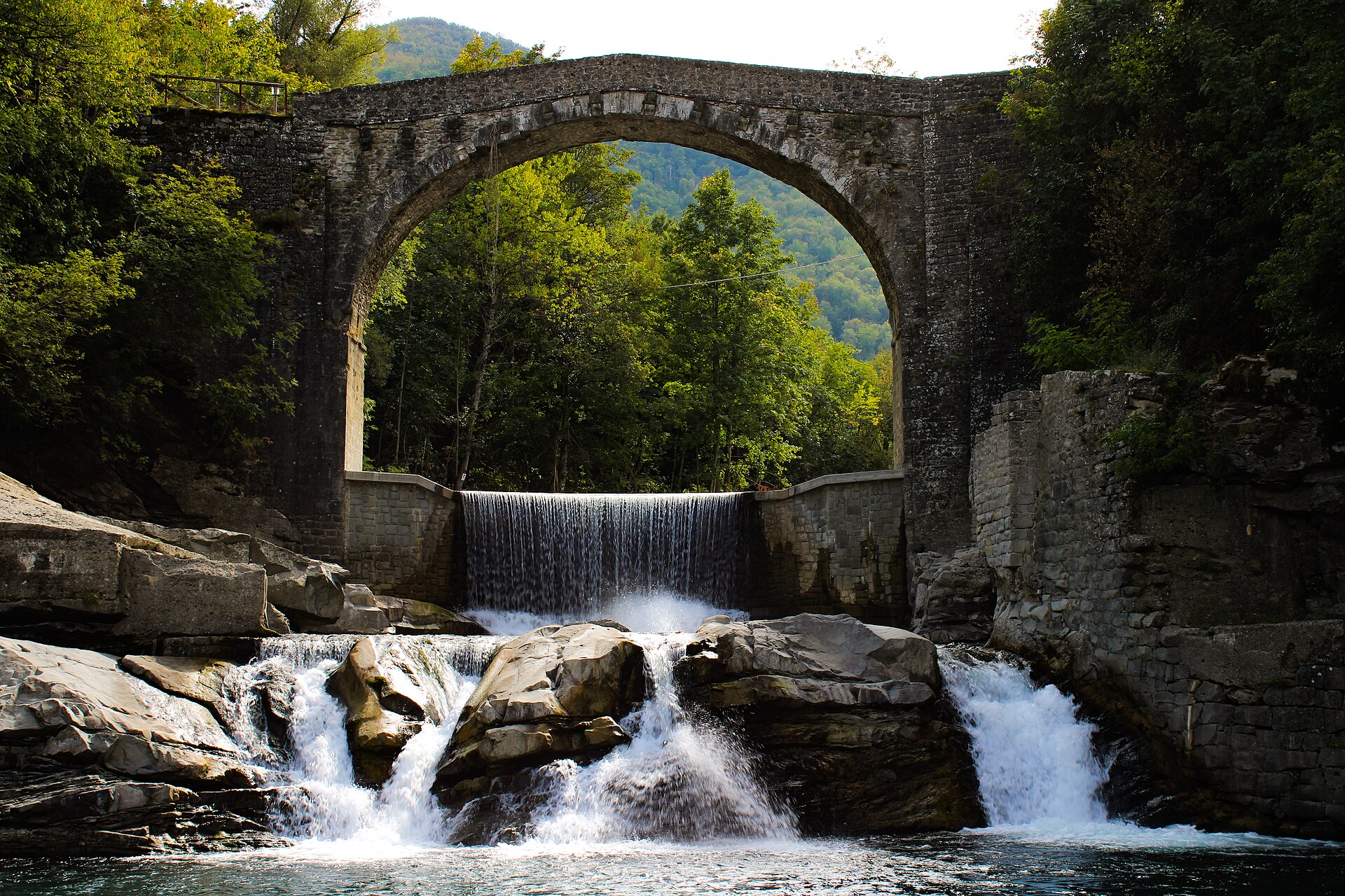 Un ponte ad arco in pietra sopra una cascata, tra i boschi di Riolunato