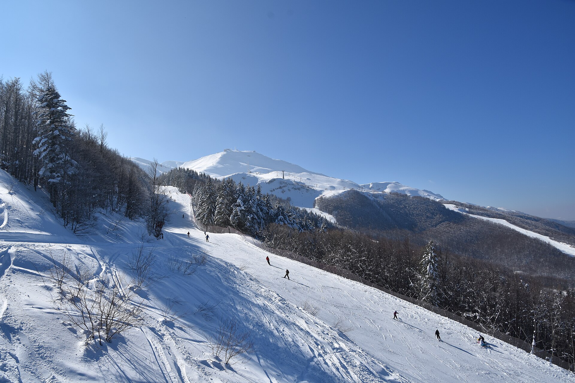 Una pista da sci innevata del comprensorio del Cimone con le montagne sullo sfondo